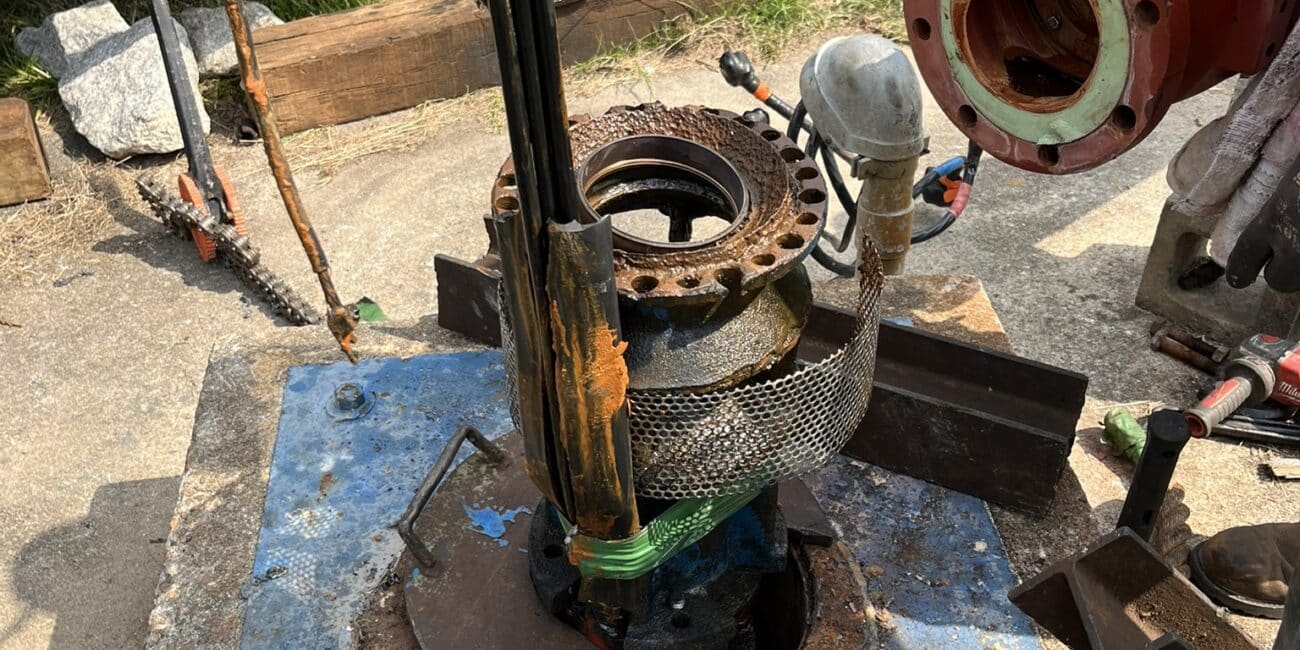 Close-up of outdoor industrial equipment being serviced; pipes, valves, fittings, a boot on a rusty blue platform with tools scattered.