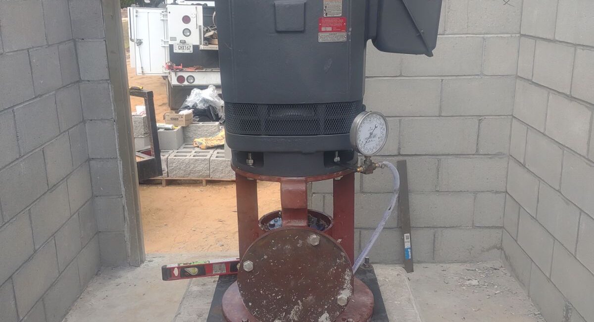 Large industrial machine on a concrete platform in a cinder block room, with construction materials and a white truck outside.